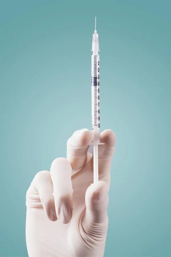 Aesthetic-Fillers-Treatment Close-up of a white-gloved hand holding a syringe against a light blue background, representing aesthetic filler services from Carolyn Zaumeyer, MSN, APRN in Fort Lauderdale.