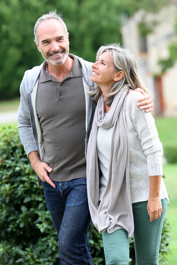 A mature couple in gray toned clothes and jeans walk happily outside, happy with their successful bioidentical hormone treatments from Carolyn Zaumeyer, MSN, APRN in Fort Lauderdale.