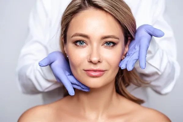 Close up of a woman's face with a doctor wearing rubber gloves standing behind her holding his hands around her face to show the amazing Botox Cosmetic treatment from Carolyn Zaumeyer, MSN, APRN in Fort Lauderdale.