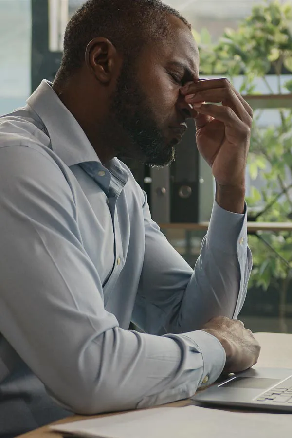 A black man rubbing the top of his nose at his desk, in need of chronic fatigue treatment from Carolyn Zaumeyer, MSN, APRN at LowTE Florida® in Greater Fort Lauderdale.