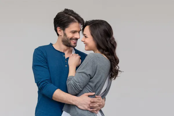 A man in a blue shirt embracing a woman in a gray shirt smiles due to his successful erectile dysfunction care from Carolyn Zaumeyer, MSN, APRN at LowTE Florida® in Greater Fort Lauderdale.