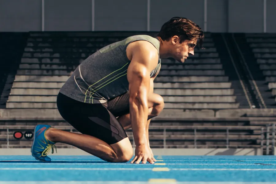 A white man kneels at the starting line on a track, determined to do his best. Get treatment for lean muscle loss and recovery from Carolyn Zaumeyer, MSN, APRN at LowTE Florida® in Greater Fort Lauderdale.