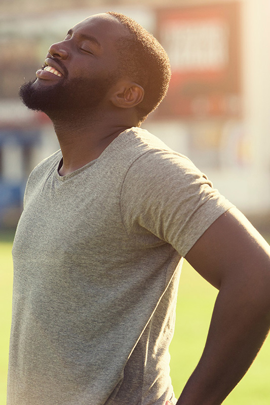 A black man in a gray t-shirt and smiles, looking up with closed eyes after a satisfying workout. Get treatment for lean muscle loss and recovery from Carolyn Zaumeyer, MSN, APRN at LowTE Florida® in Greater Fort Lauderdale.