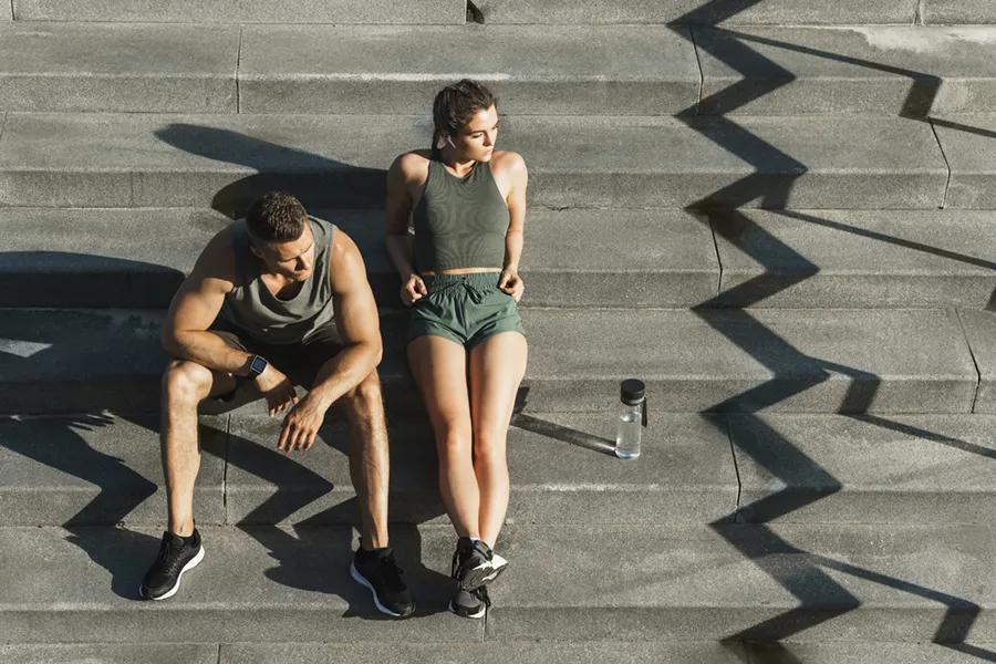A couple in gray and green track clothes resting after a workout on stone steps, happy with their weight loss plans from Carolyn Zaumeyer, MSN, APRN in Fort Lauderdale.
