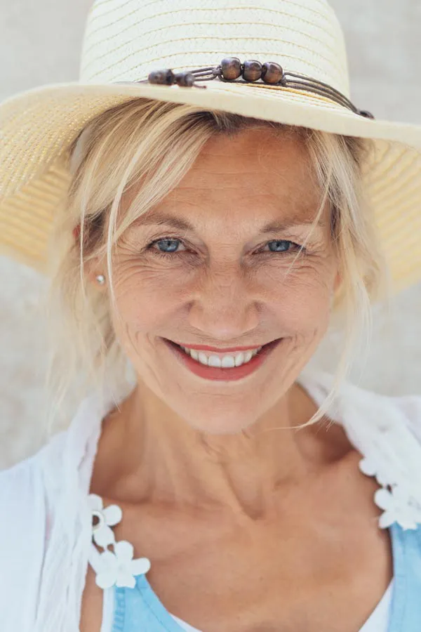 A beautiful, smiling older woman with blonde hair and a sunhat, happy with menopause treatment from Carolyn Zaumeyer, MSN, APRN at LowTE Florida® in Greater Fort Lauderdale.