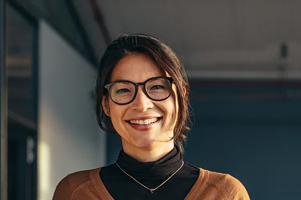 A brunette woman with glasses smiles in a gray-blue walled office. Get metabolic syndrome from Carolyn Zaumeyer, MSN, APRN at LowTE Florida® in Greater Fort Lauderdale.