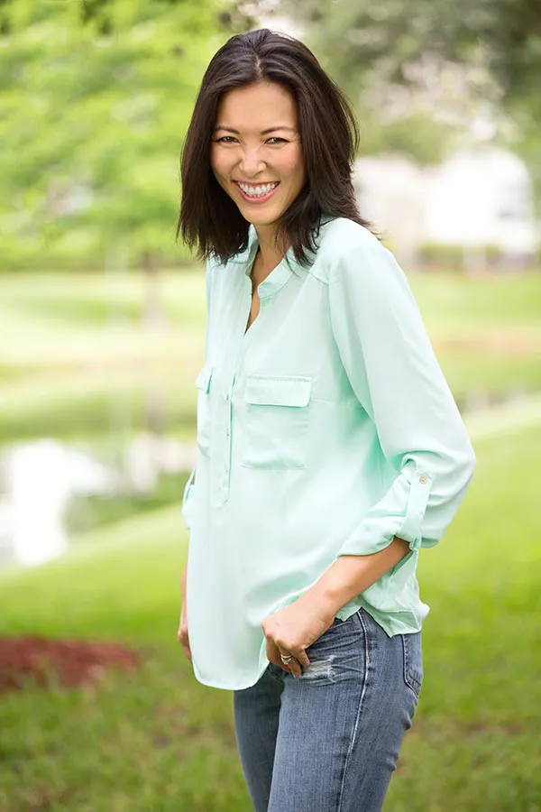 A middle-aged brunette woman in a light green button-up shirt stands outside smiling, happy with her perimenopause treatment from Carolyn Zaumeyer, MSN, APRN at LowTE Florida® in Greater Fort Lauderdale.