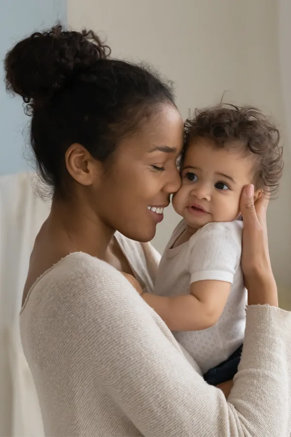 A black woman happily touches her forehead to her infant's head. Get treatment for postpartum hormone imbalance from Carolyn Zaumeyer, MSN, APRN at LowTE Florida® in Greater Fort Lauderdale.