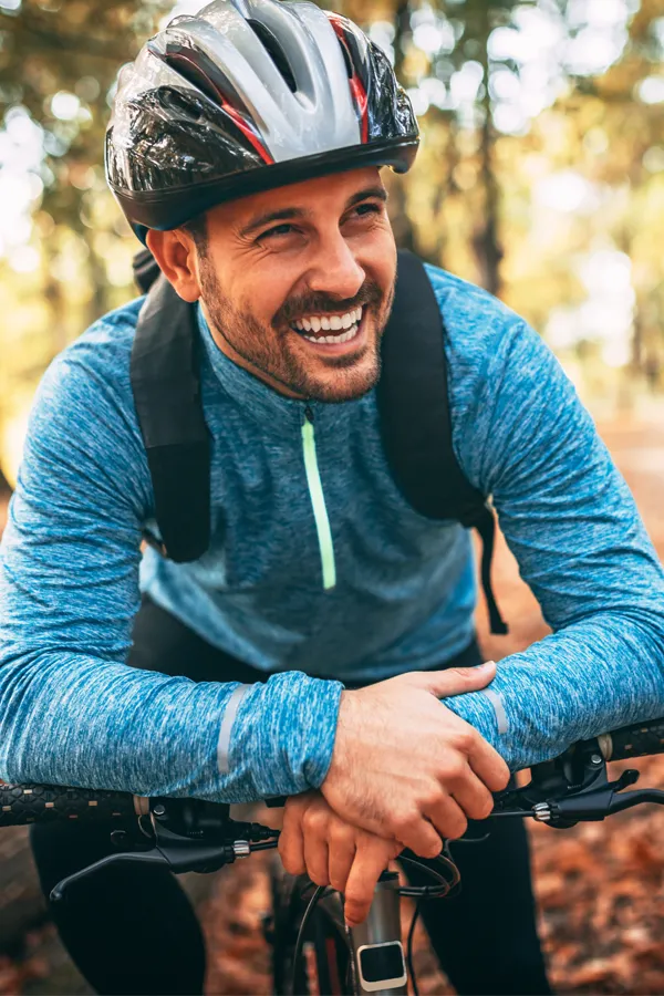 A middle-aged man on a trail in cycling clothes is smiling and leaning on his bike's handlebars. Get testosterone for Low T from Carolyn Zaumeyer, MSN, APRN at LowTE Florida® in Greater Fort Lauderdale.