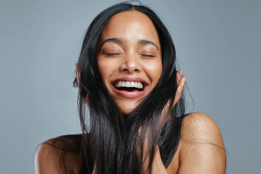 Viviscal-for-Womens-Hair-Loss-Clinic A smiling woman runs her fingers through her long, thick black hair. Get Viviscal for women's hair restoration from Carolyn Zaumeyer, MSN, APRN in Fort Lauderdale.