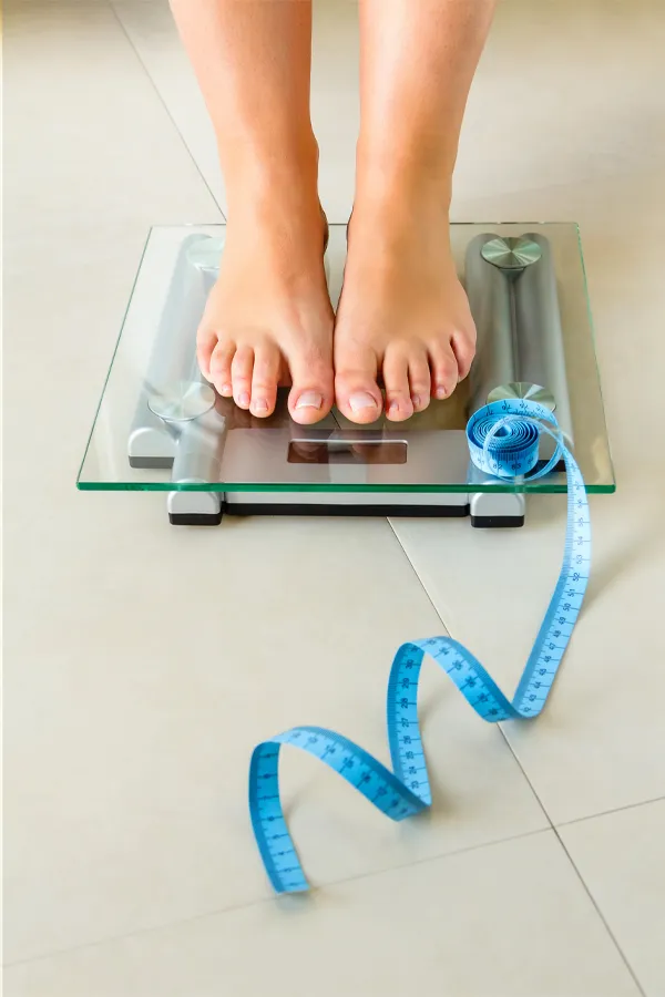 Close-up of a woman's feet standing on a scale, with measuring tape by her toes, getting treatment for weight loss resistance from Carolyn Zaumeyer, MSN, APRN at LowTE Florida® in Greater Fort Lauderdale.
